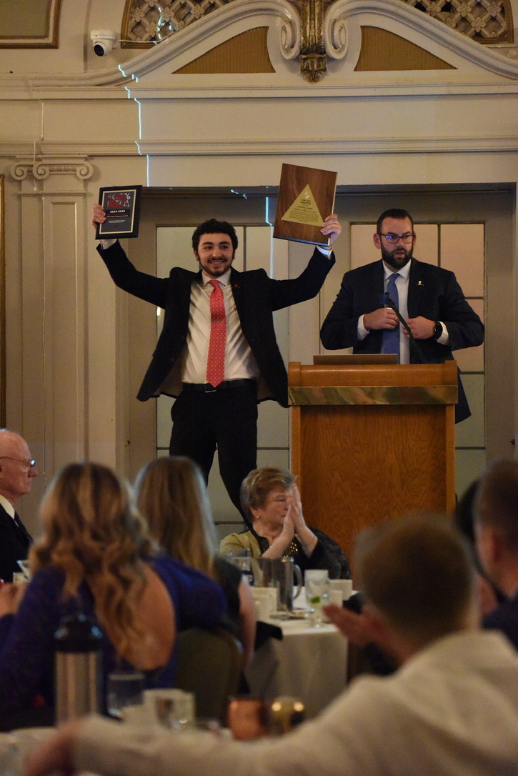 A brother jumping on a chair celebrating with the award plaques raised high